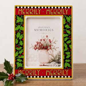 May include: A rectangular picture frame with a red border featuring the text MERRILY MERRILY in yellow. The sides have a green holly and red berry pattern on a black background. The frame contains a print with the text HOLIDAY MEMORIES.