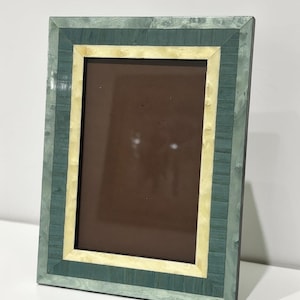 May include: Rectangular picture frame with a green and cream-colored mosaic design. The frame has a dark brown interior and is set against a white background. The frame's design features a layered effect with a light green outer border and a cream-colored inner border.