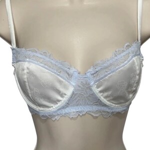 May include: White satin bra with a floral pattern and pale blue lace trim. The bra has adjustable straps and a classic design. The lace detailing adds a delicate touch to the lingerie.