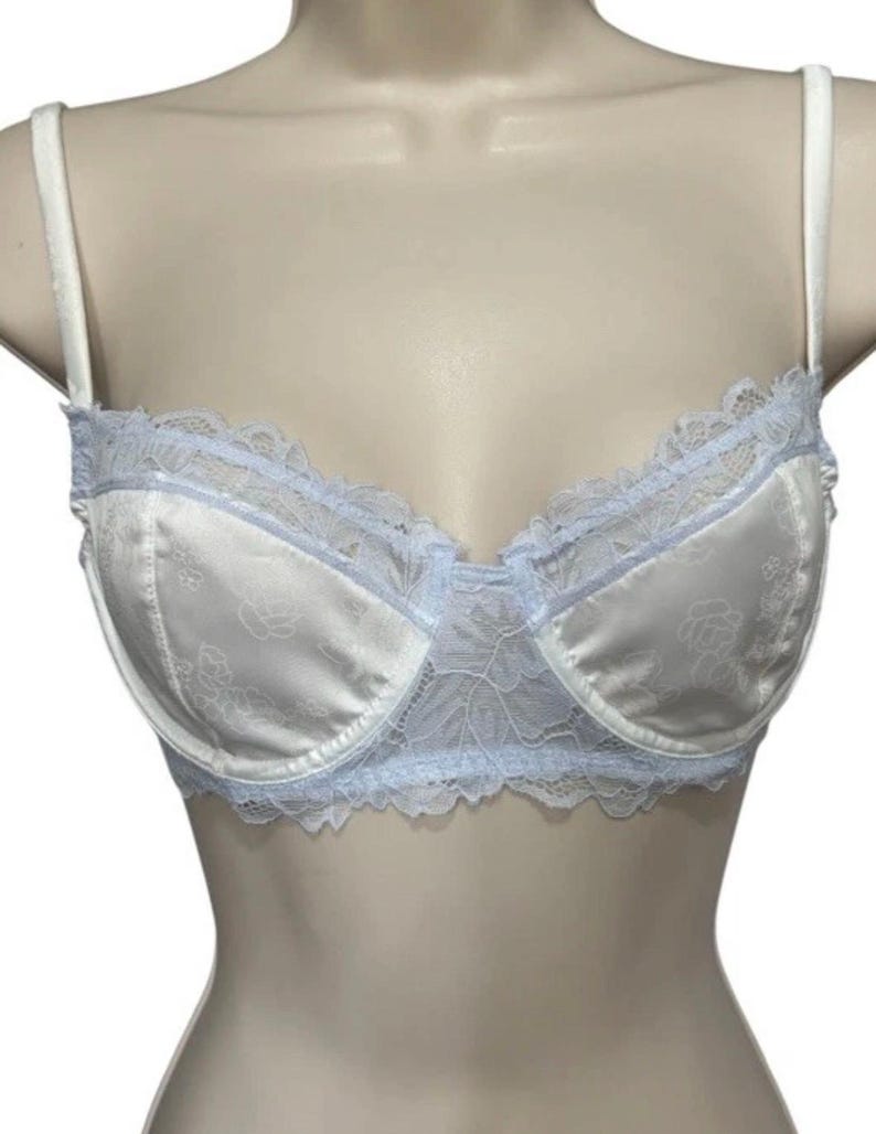 May include: White satin bra with a floral pattern and pale blue lace trim. The bra has adjustable straps and a classic design. The lace detailing adds a delicate touch to the lingerie.