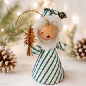 May include: A decorative figurine featuring a person wearing a blue and white striped cone-shaped hat and matching dress with a white faux fur collar. The face has star-shaped eyes and a red star mouth, holding a small gold bottle brush tree.