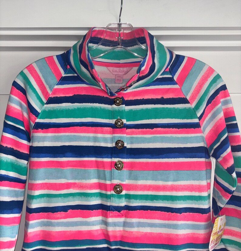 May include: A long-sleeved shirt with a colorful striped pattern in shades of pink, blue, green, and white. The shirt features a collared neckline and is fastened with decorative gold buttons. The garment is hanging on a clear hanger.