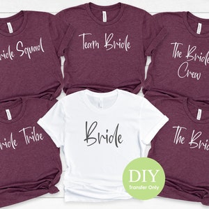 May include: Set of six t-shirts with different text designs for a bridal party. The shirts are in maroon and white with the text "Bride Squad", "Team Bride", "The Bride's Crew", "Bride Tribe", "The Bride", and "Bride" in white.