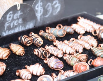 May include: A variety of crystal pendants wrapped in copper wire. The crystals are in various colors and shapes, including clear, pink, green, and blue. The pendants are displayed on a black surface with a sign that says "Get Free Worldwide Shipping".