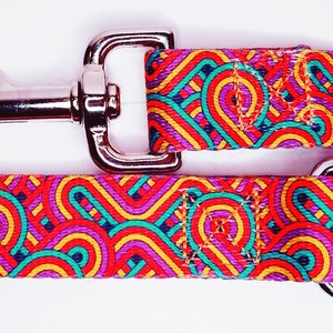 May include: A colorful dog leash with a geometric pattern in shades of red, orange, yellow, green, blue, and purple. The leash has a silver clip and a silver D-ring.