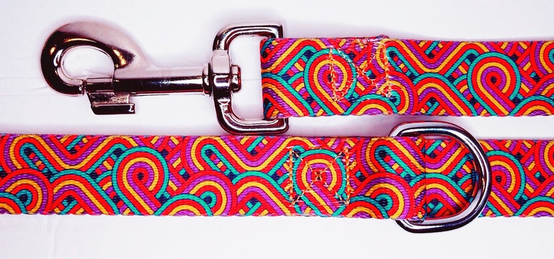 May include: A colorful dog leash with a geometric pattern in shades of red, orange, yellow, green, blue, and purple. The leash has a silver clip and a silver D-ring.