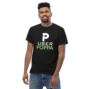 May include: Black t-shirt with the text "UBER POPPA" in white and green. The design features a large white "P" above the word "UBER". The word "POPPA" is in green. The t-shirt is made of a soft material.