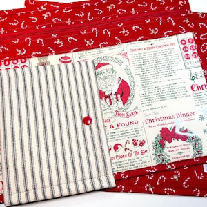 May include: A rectangular fabric pouch with a red candy cane print and a zipper closure, featuring a cream-colored panel with vintage-style Christmas text and Santa graphics, layered with a smaller black and white striped fabric envelope.