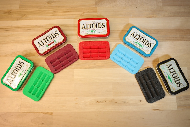 May include: An assortment of Altoids mint tins and colorful, rectangular trays. The tins are red, green, blue, and silver, with text labels. The trays are red, green, blue, burgundy, and black, each with ten rectangular slots.