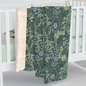 May include: A dark blue and green floral patterned blanket with a cream-colored sherpa lining. The blanket features a repeating pattern of stylized flowers and leaves in shades of green and blue. The blanket is draped over a white crib.
