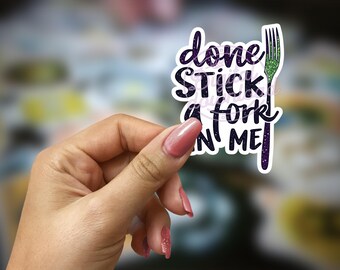 Op de afbeelding: Een sticker met een paars en groen glitterontwerp met de tekst "done stick a fork in me".