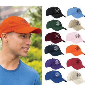 May include: A selection of 12 blank baseball caps in various colors, including black, blue, green, red, orange, white, beige, pink, purple, and navy. Each cap features a circular area for embroidery or screen printing with the text "YOUR LOGO HERE" in a white circle.