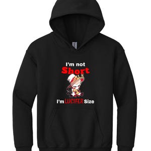 Puede incluir: Sudadera con capucha negra con un estampado gr&aacute;fico blanco de un personaje de dibujos animados con una corona y sosteniendo un coraz&oacute;n. El texto "I'm not Short I'm LUCIFER Size" est&aacute; impreso en rojo.