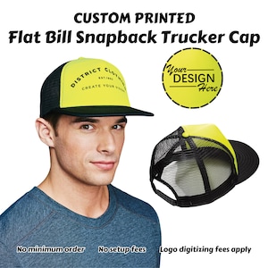 May include: A yellow and black trucker cap with a flat bill. The front of the cap has a black logo that says "District Clothing Est. 1983 Create Your Vision". The back of the cap has a yellow mesh panel. The cap is shown on a model wearing a blue shirt. The text "Your Design Here" is shown in a circle on a yellow background.