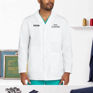 May include: A white lab coat with long sleeves, a notched collar, and a button-down front. The text DOCTOR is printed in black on the right chest, and MAY CUSTOM is printed in black above the left chest pocket. A teal shirt is visible underneath.