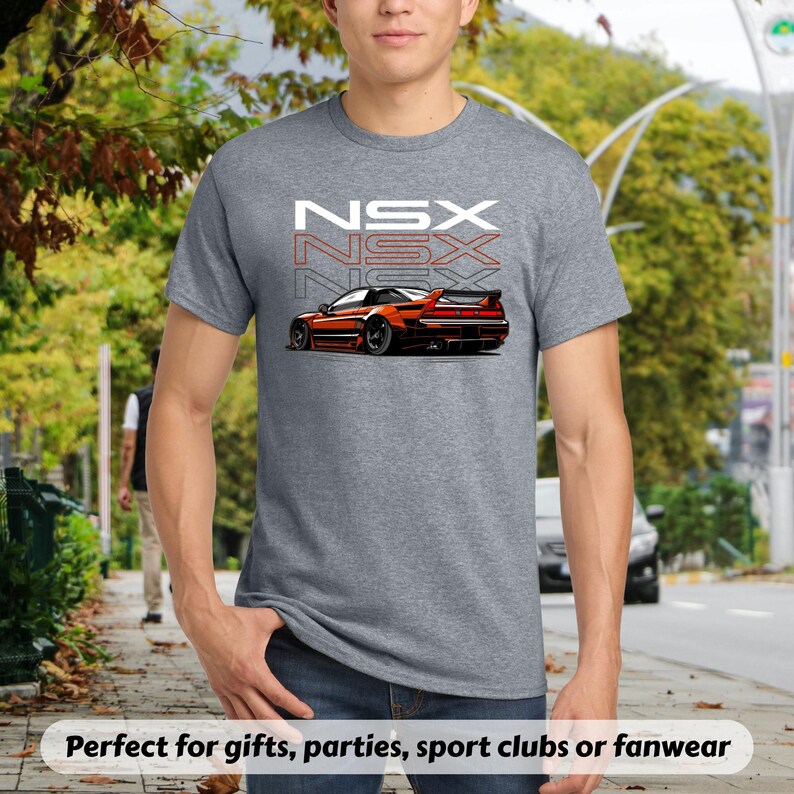 May include: A gray t-shirt featuring a stylized orange sports car graphic with the word "NSX" stacked three times in white and red. The shirt is made of a soft material and is suitable for casual wear.