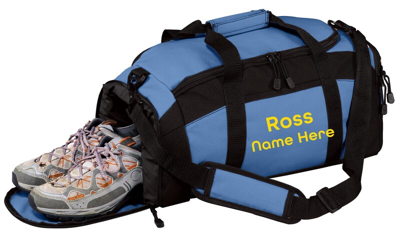 May include: A blue and black duffel bag with a dedicated side shoe compartment containing a pair of grey and orange athletic sneakers. The bag features black webbing straps, a padded shoulder strap, and the yellow text Ross Name Here.