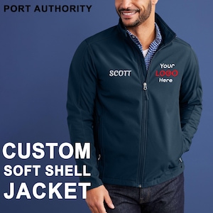 May include: Navy blue custom soft shell jacket with the text "PORT AUTHORITY" at the top. The jacket has a zipper closure and two pockets. The name "SCOTT" is embroidered on the left chest, and the words "Your LOGO Here" are on the right chest.