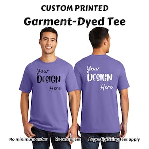 May include: A purple garment-dyed t-shirt with the text "Your Design Here" printed on the front and back. The shirt is being modeled by a person.