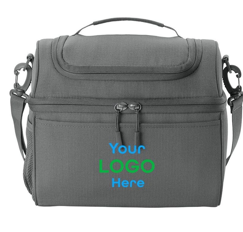 以下が含まれることがあります： グレーの断熱ランチバッグ。上部にハンドル、取り外し可能なショルダーストラップ付き。バッグにはジッパー付きのメインコンパートメントとフロントポケットがあります。「Your LOGO Here」の文字が青と緑でプリントされています。