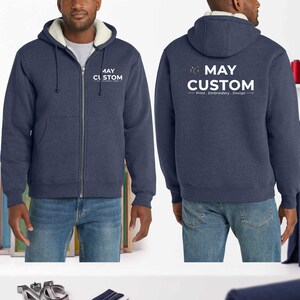 May include: A navy blue zip-up hoodie with a white sherpa lining, featuring a drawstring hood and front pockets. The chest displays the text MAY CUSTOM, while the back features the logo and text MAY CUSTOM Print . Embroidery . Design.