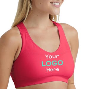 May include: A vibrant red sports bra with a scoop neckline. The bra features the text "Your LOGO Here" in white and teal. The material appears to be a breathable, athletic fabric.