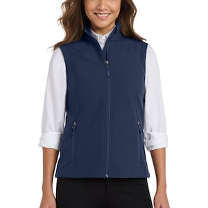 May include: A navy blue sleeveless waistcoat featuring a full-length front zip, a stand-up collar, and two side pockets with zip closures. The waistcoat is worn over a white long-sleeved collared shirt with the sleeves rolled up to the elbows.