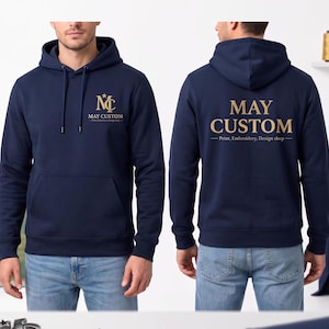 May include: A navy blue hooded sweatshirt featuring a gold logo on the front chest with the text "MC MAY CUSTOM Print, Embroidery, Design shop". The back displays the text "MAY CUSTOM Print, Embroidery, Design shop" in large gold lettering.