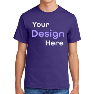 May include: A purple t-shirt with the text "Your Design Here" in white and light purple. The shirt has short sleeves and a crew neck. The t-shirt is made of a soft material.