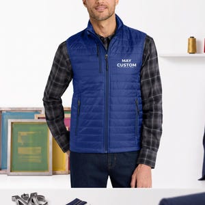May include: A royal blue quilted puffer vest featuring a full-length front zipper, a stand-up collar, and two side zippered pockets. The chest area displays the white printed text MAY CUSTOM. The vest is worn over a grey and black plaid long-sleeve shirt.