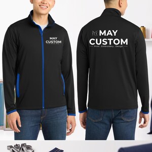 May include: A black full-zip jacket with blue trim on the collar, zipper, and cuffs. The front features the white text MAY CUSTOM Print. Embroidery. Design. The back displays the same logo in a larger size with the MC monogram icon above it.