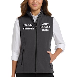 May include: A charcoal grey softshell vest featuring a full-length black front zip, a stand-up collar, and two zipped side pockets. The chest area displays white embroidered text reading Mandy MSN APRN on the right and YOUR LOGO HERE on the left.