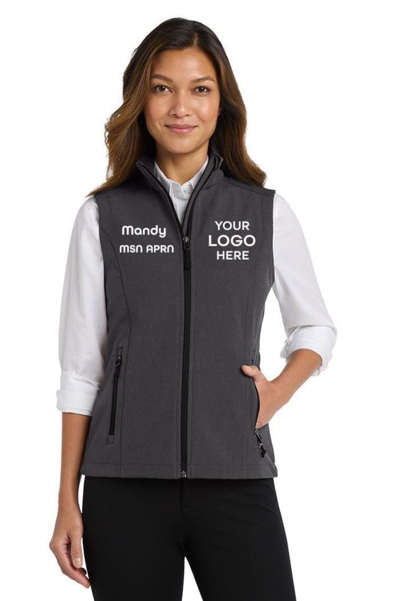 May include: A charcoal grey softshell vest featuring a full-length black front zip, a stand-up collar, and two zipped side pockets. The chest area displays white embroidered text reading Mandy MSN APRN on the right and YOUR LOGO HERE on the left.