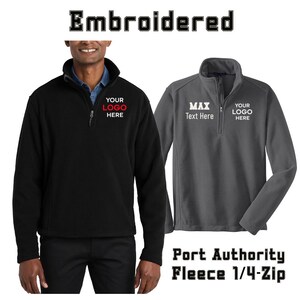 May include: A black and a charcoal gray Port Authority fleece 1/4-zip pullover. The black pullover features the text "YOUR LOGO HERE" in red and white. The gray pullover features the text "MAX Text Here" and "YOUR LOGO HERE" in white.