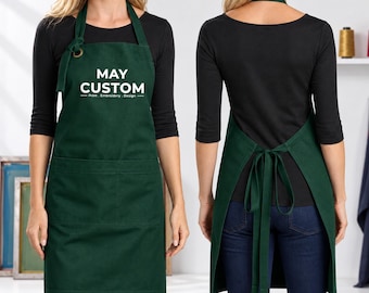 May include: A dark green apron featuring a neck strap with a metal grommet and two front pockets. The chest area displays the white text MAY CUSTOM Print . Embroidery . Design. The back view shows a neck strap and long ties secured in a bow at the waist.