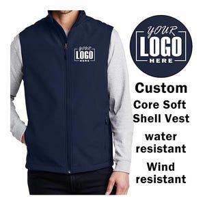 May include: A navy blue soft shell vest with a zipper closure. The vest is water and wind resistant. The vest has a logo that says "YOUR LOGO HERE" on the left chest.