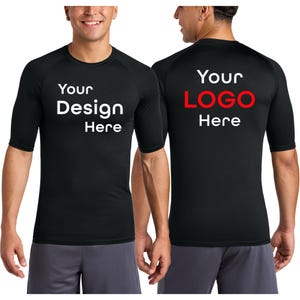 May include: Black short-sleeved athletic shirt with the text "Your Design Here" on the front and "Your LOGO Here" on the back. The shirt is worn by a person in gray shorts.