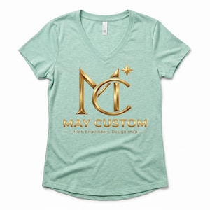May include: A light green V-neck t-shirt featuring a metallic gold logo with the letters MC and a small star. Below the logo, the text reads MAY CUSTOM, followed by the smaller text Print, Embroidery, Design shop, centered on the chest.