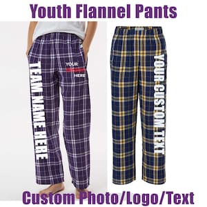 May include: Two pairs of youth flannel pants. One pair is purple with a white plaid pattern and the text "TEAM NAME HERE" on the side. The other pair is navy blue with a yellow plaid pattern and the text "YOUR CUSTOM TEXT" on the side. The image also includes the text "Custom Photo/Logo/Text".