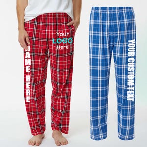 May include: Red plaid pajama pants with the text "NAME HERE" vertically down the left leg and "Your LOGO Here" on the pocket. Blue plaid pajama pants with the text "YOUR CUSTOM TEXT" vertically down the right leg.