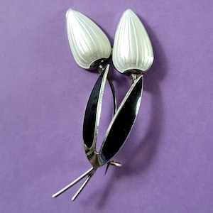 Peut inclure: Une broche en argent et émail noir en forme de deux tulipes stylisées. Les tulipes sont blanches avec des tiges et des feuilles noires.