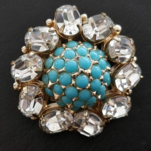 May include: A gold-toned brooch with a turquoise center surrounded by clear rhinestones.