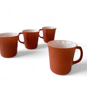 May include: Set of four orange mugs with white interiors. The mugs are made of glass and have a rounded shape.