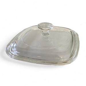 May include: Clear glass lid with a knob on top. The lid is square shaped with rounded edges.