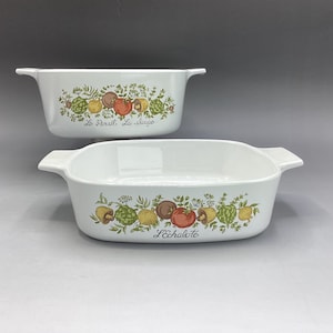 May include: Two white ceramic baking dishes with green and brown floral designs. The smaller dish has the text "Le Persil La Sauge" and the larger dish has the text "L'Echalote".