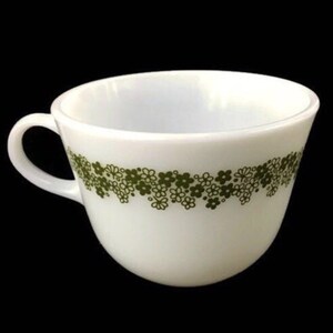 May include: White ceramic mug with a green floral pattern around the rim. The mug has a rounded shape and a handle.