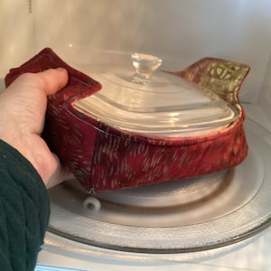 May include: A red and green fabric microwave bowl cozy with a glass baking dish inside.