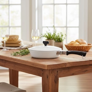 May include: A white, lidded skillet with a black handle sits on a wooden table, alongside a basket of bread, wine glasses, and potted herbs. The kitchenware is set for a meal.