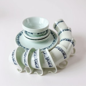 May include: A complete dinnerware set in a light blue hue, featuring plates, bowls, and cups. Each piece is adorned with a dark blue floral pattern around the rim. The cups have a unique handle design.