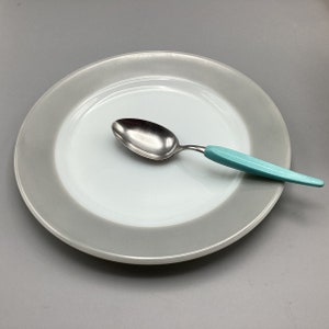 May include: A white plate with a gray rim and a silver spoon with a turquoise handle.